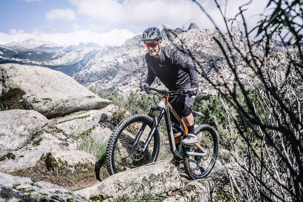 Motociclista maduro escalando colina rocosa con bicicleta de montaña
. - Foto, Imagen
