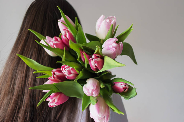 A woman hides a bouquet of tulips behind her back.  - Foto, imagen