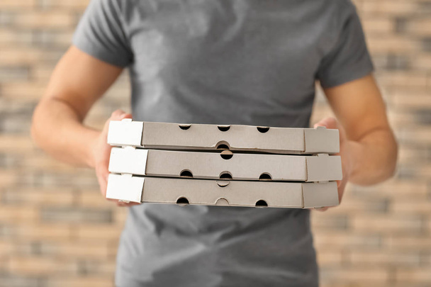 Доставщик с картонными коробками пиццы на фоне кирпичной стены
 - Фото, изображение