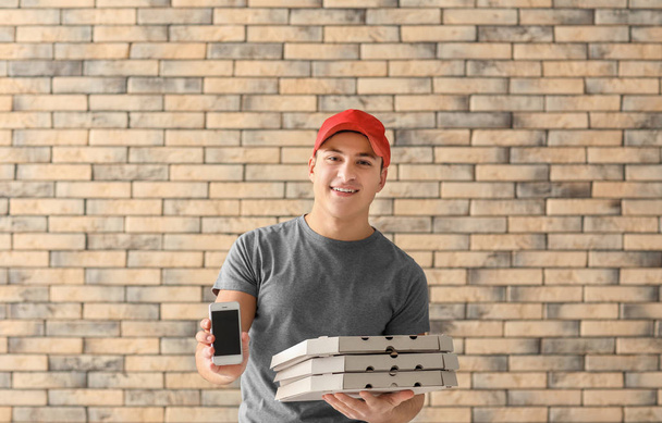 Entrega homem com caixas de pizza de papelão e telefone no fundo da parede de tijolo
 - Foto, Imagem