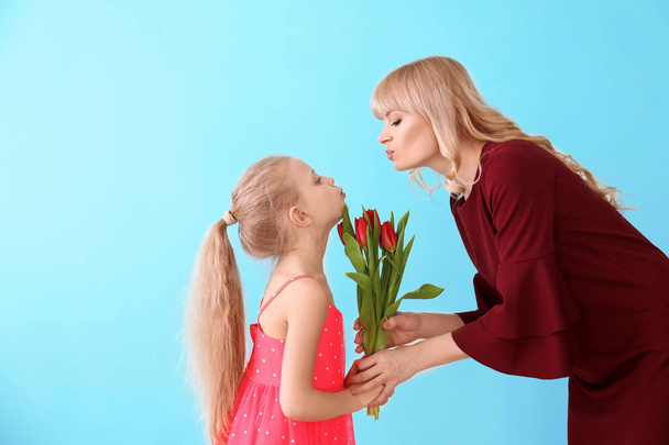 Portrait of cute little girl and her mother with tulip bouquet on color background - Foto, Bild