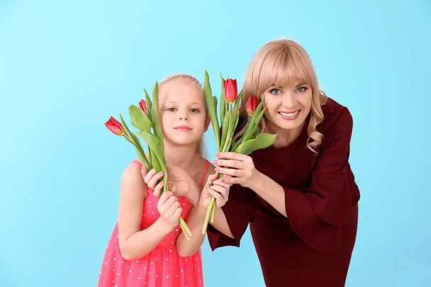 Портрет милой маленькой девочки и ее матери с тюльпанами на цветном фоне
 - Фото, изображение