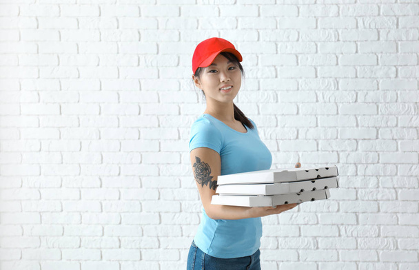 Ασιατικές γυναίκα με κουτιά από χαρτόνι πίτσας σε φόντο τοίχο τούβλου. Υπηρεσία παράδοσης τροφίμων - Φωτογραφία, εικόνα