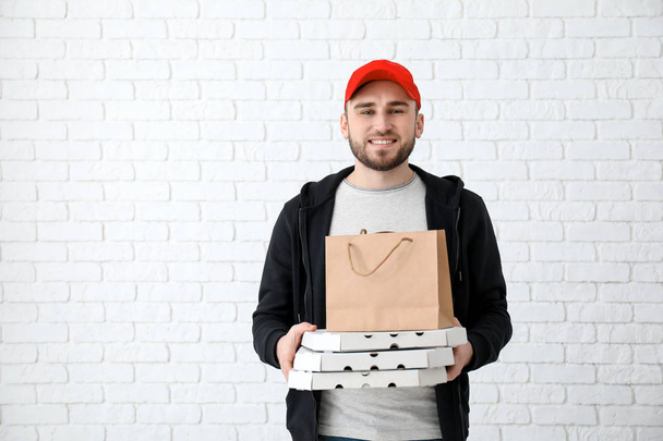 Young man with cardboard pizza boxes and paper bag on brick wall background. Food delivery service - Photo, Image