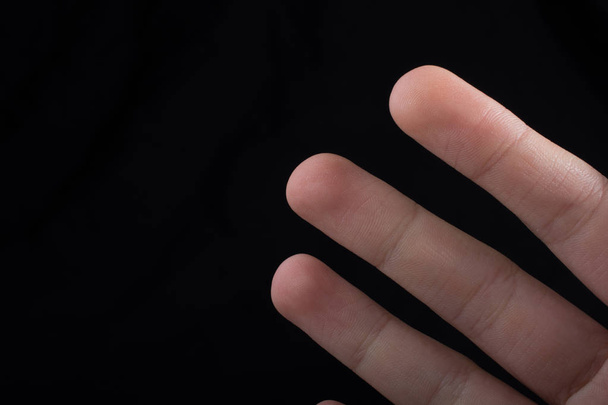 Trois doigts d'une main d'enfant en partie vus en fond noir - Photo, image