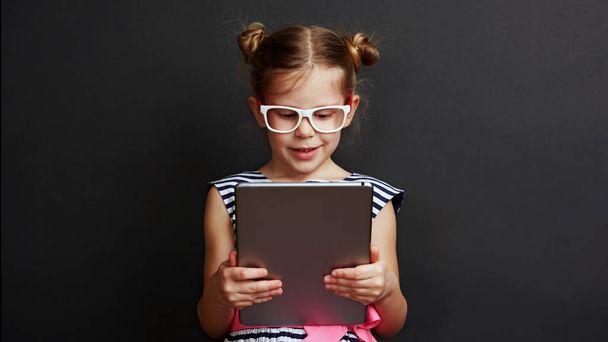 Adorable girl playing game on digital tablet over dark background. Technology and lifestyle. - Foto, Imagem