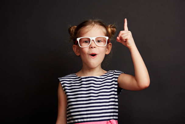 Child having idea. Pretty girl in glasses posing with finger up over blackboard. - Foto, Imagem