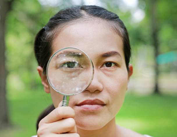 Asian woman with a magnifying glass on eye in the garden - Photo, Image