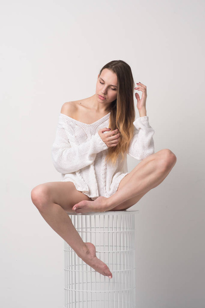 junges schönes Mädchen posiert im Studio, sitzt im weißen Pullover auf einem Stuhl - Foto, Bild