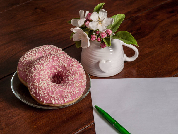 daruje na průhledné talíře, bílá váza s růžovými květy, bílý list papíru pro psaní a zelené pero - Fotografie, Obrázek
