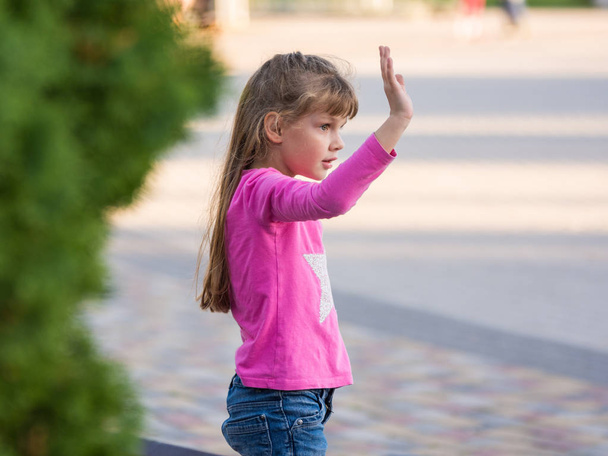 Niña de seis años agitando su mano, vista lateral
 - Foto, Imagen