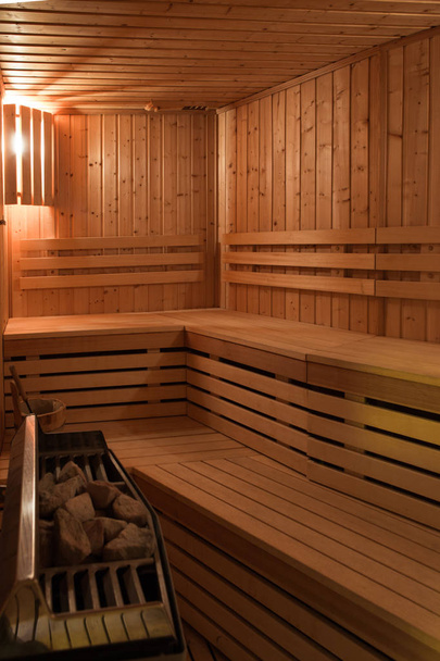Innenraum einer kleinen hölzernen Sauna mit Sitzgelegenheiten und Ofen.  - Foto, Bild
