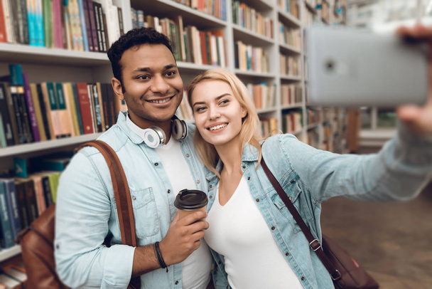Ethnic indian mixed race guy and white girl in library and taking selfie on smartphone - Foto, Imagem