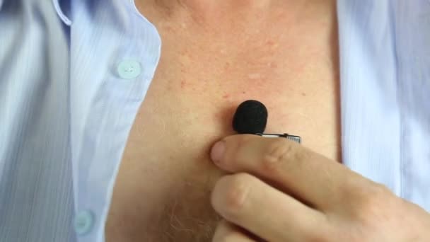 A man attaches a hidden microphone to his chest with an adhesive tape.A private detective puts on a small microphone a buttonhole under his shirt for secret recording of the sound. - Materiał filmowy, wideo