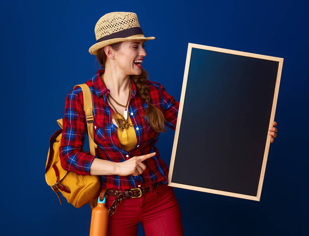 happy healthy woman hiker in a plaid shirt pointing at blank board against blue background - Fotoğraf, Görsel
