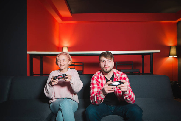 Couple of young people, a man and a girl playing video games on the console. A couple is sitting on the couch with joysticks in her hands and playing games - Photo, Image