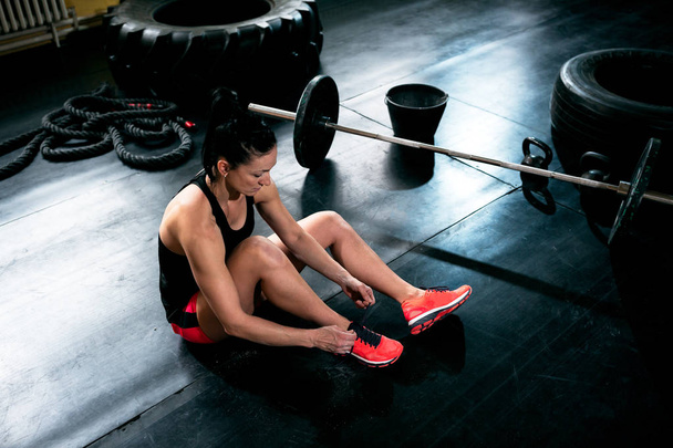 Female fit girl resting and bins sneakers and prepare for exercise at crossfit gym - Foto, afbeelding