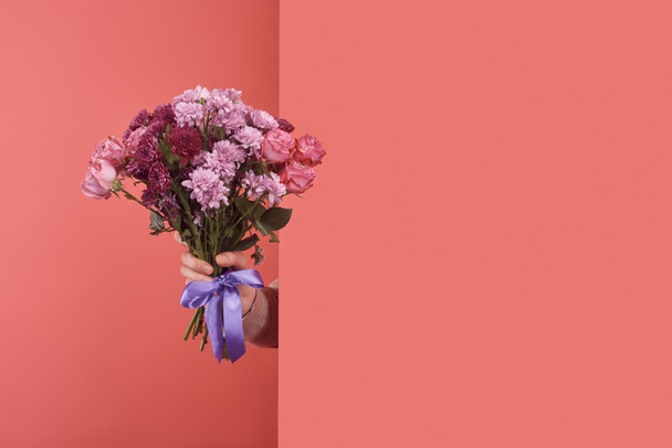woman sticking out flowers bouquet behind wall on red - Foto, Imagen