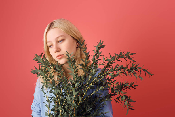 вдумчивая молодая женщина с кучей эвкалиптовых ветвей, изолированных на красном
 - Фото, изображение