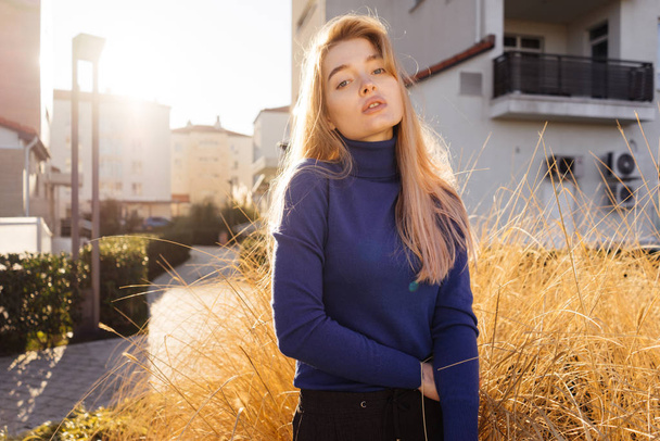 stylish beautiful blond model girl in blue sweater posing on open air in the sun - Photo, image