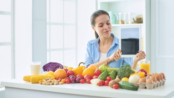 feliz ama de casa joven sentada en la cocina preparando alimentos a partir de una pila de diversas frutas y verduras orgánicas frescas
 - Foto, Imagen