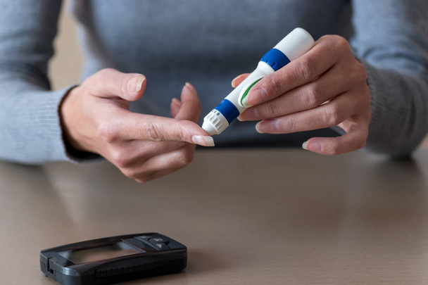 Close-up of woman hands using lancet on finger to check blood sugar level by Glucose meter.  - Fotografie, Obrázek