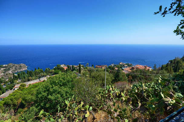 Таормина, Италия, Сицилия 26 августа 2015 года. Великолепная панорама от греческого театра к морю. Пышная природа, средиземноморская растительность, цветы. Море и лодки
. - Фото, изображение