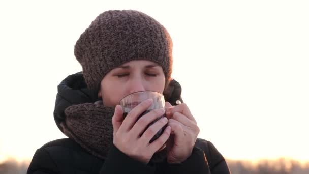 Woman warms you with cup of hot tea and smiles. Drink tea in open frosty air. - Footage, Video
