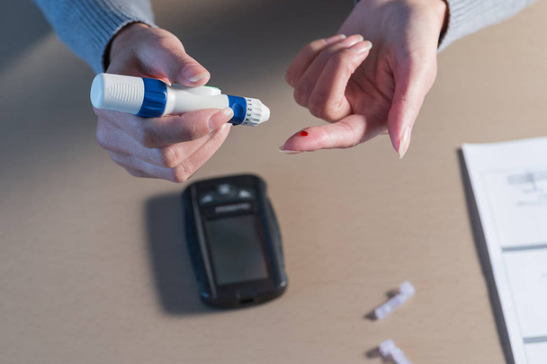 Close-up of woman hands using lancet on finger to check blood sugar level by Glucose meter.  - Foto, Imagem