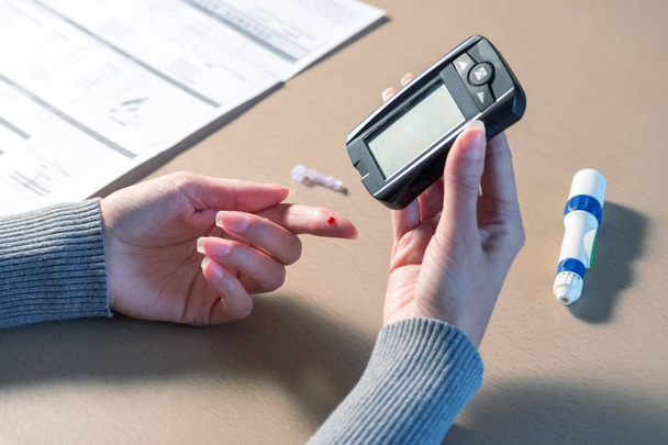 Close-up of woman hands using lancet on finger to check blood sugar level by Glucose meter.  - Fotó, kép