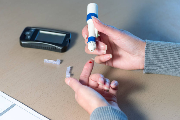 Close-up of woman hands using lancet on finger to check blood sugar level by Glucose meter.  - Foto, Imagem