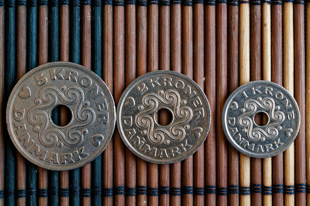 Три монеты Дании номиналом 5, 2 и 1 крона (корона) лежат на деревянном бамбуковом столе, хорошо для фона или открытки
 - Фото, изображение