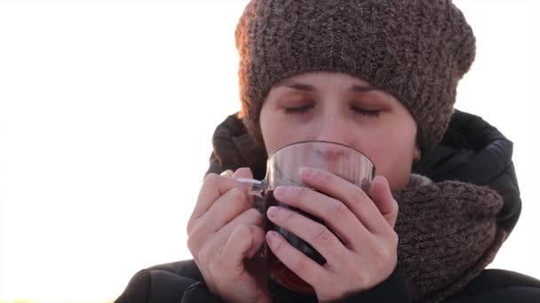 Красивая замороженная девушка пьет чай из прозрачного стекла на открытом воздухе
. - Кадры, видео