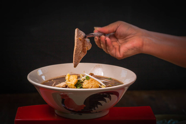 Hand uses chopsticks to pickup tasty noodles on black background - Valokuva, kuva