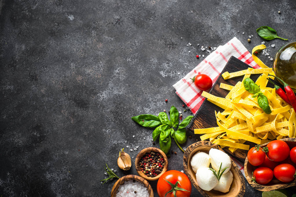 Makaronivalmisteet, tomaatit, juusto, basilika ja oliiviöljy mustalla kivitaululla
 - Valokuva, kuva