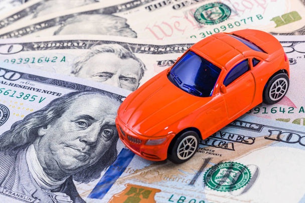 Close-up rode auto speelgoed op dollar bill achtergrond. Concept van autoverzekering - Foto, afbeelding
