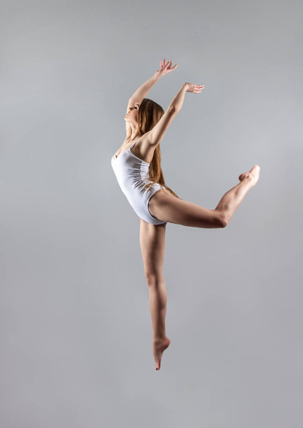a young slender girl gymnast jumps high in the dance. Gray background. - Foto, Imagen