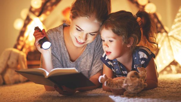 mother and child daughter reading a book and a flashlight before - Foto, Imagen