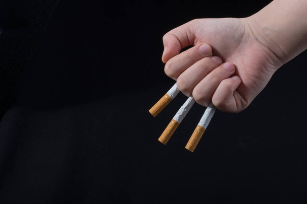 La mano tiene le sigarette tra le dita su sfondo nero
 - Foto, immagini