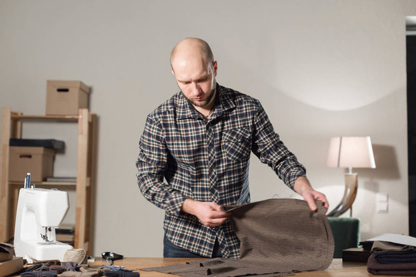 Le tailleur pose le tissu de laine sur la table de découpe. Jeune homme travaillant comme tailleur et utilisant une machine à coudre en atelier
. - Photo, image