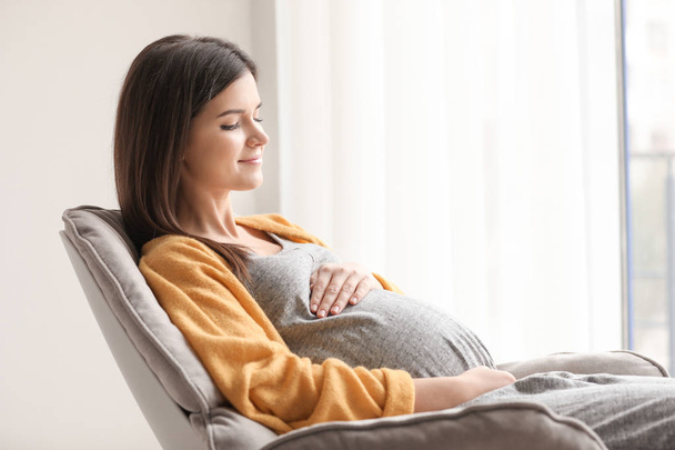 Young pregnant woman resting in armchair at home - Foto, Bild