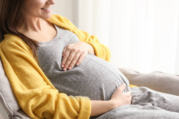 Νεαρή έγκυος γυναίκα που αναπαύεται στην πολυθρόνα στο σπίτι - Φωτογραφία, εικόνα