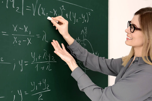 Young female teacher writing on blackboard in classroom - Foto, imagen