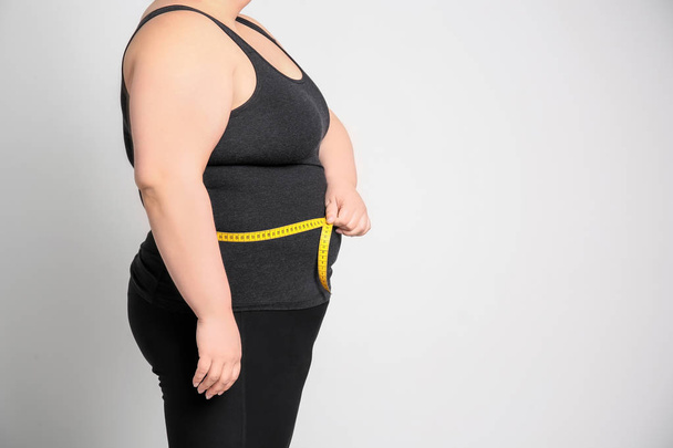 Overweight woman with measuring tape on light background - Foto, afbeelding
