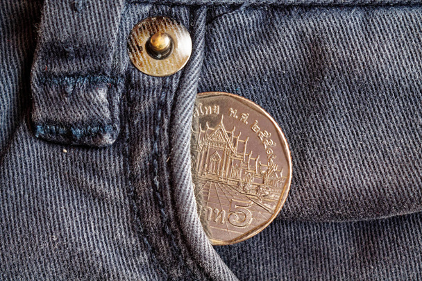 Moneda tailandesa con una denominación de cinco baht en el bolsillo de vaqueros azules obsoletos
 - Foto, imagen