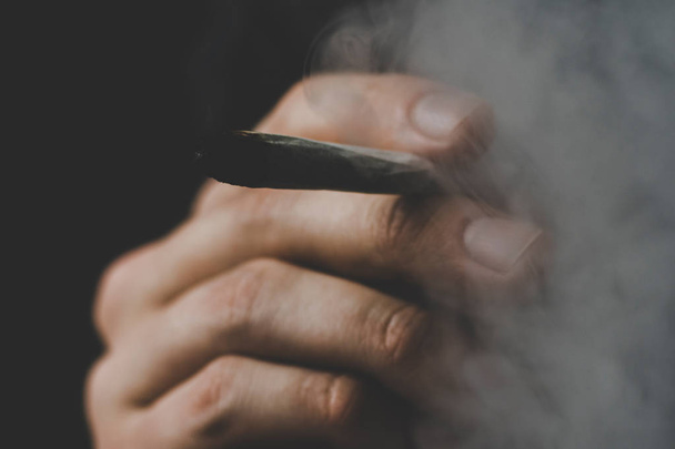 joint in hand. A man smokes cannabis weed, a . Smoke on a black background. Concepts of medical marijuana use and legalization of the cannabis. - Valokuva, kuva