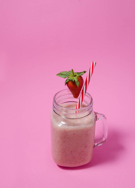 Pink strawberry smoothie in a mason jar glass with straw and scattered berries on pink background. Healthy and delicious breakfast. Organic Strawberry Smoothie made with fresh Ingredients. - Fotografie, Obrázek