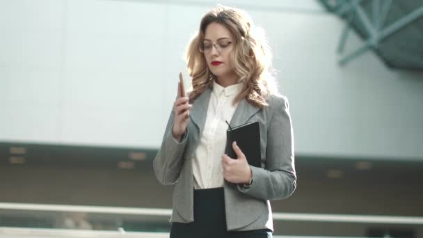 fiatal nő, egy öltöny teszi a hívást a mobiltelefonján. portréja egy üzleti nő egy lobbi egy irodaház - Felvétel, videó