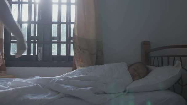 Child sleeps in dark room. Mother comes, opens the curtains and waking up her. - Filmati, video