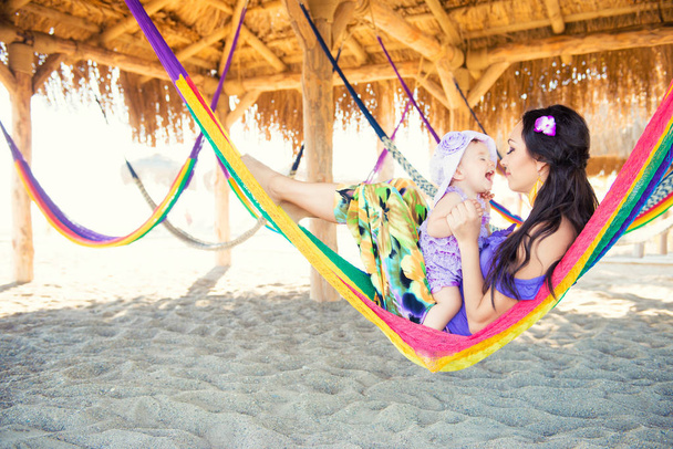 happy stylish family with cute daughter relaxing in hammock on summer vacation in evening sun light on the beach. hipster couple with child resting and having fun in sunset. - Фото, зображення